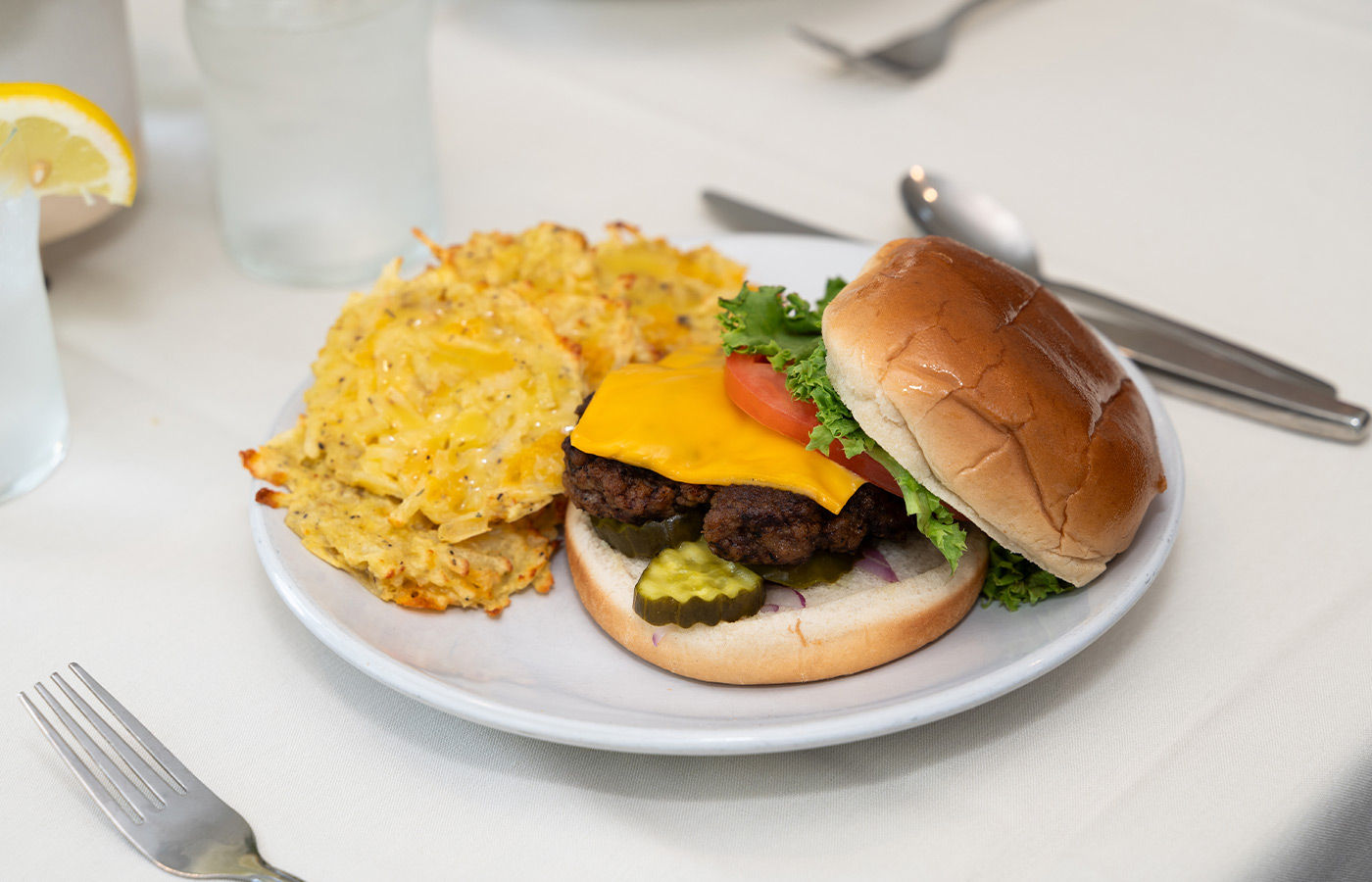 A plate with a burger and hashbrowns on it.