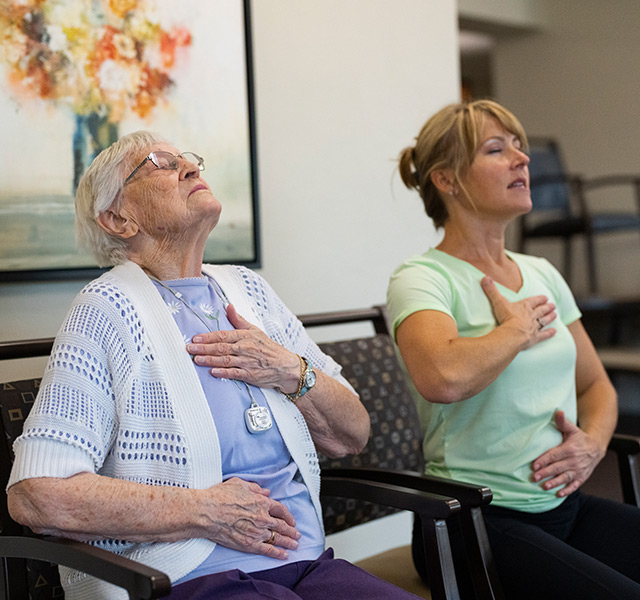 A resident is practicing their breathing exercises alongside their caregiver.