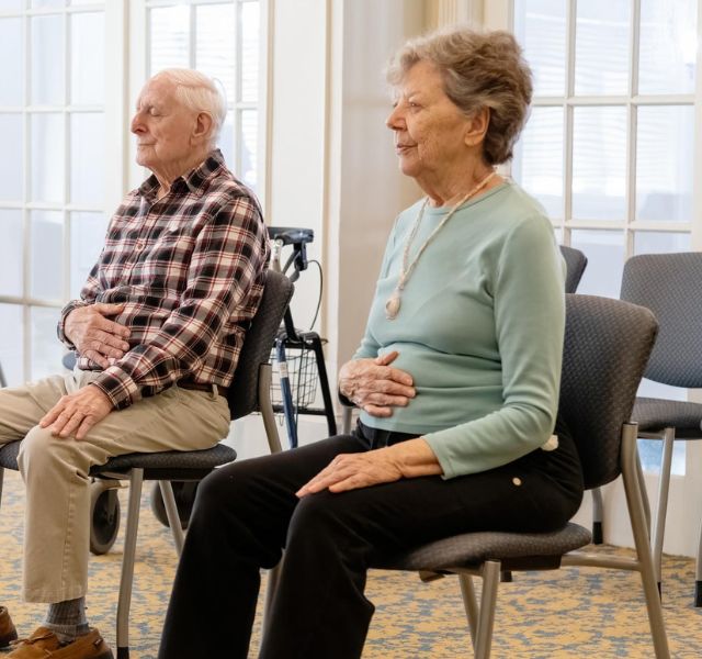 Two residents sitting in chairs with hands on their stomachs.