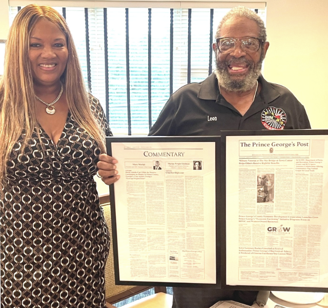 Two people holding up a framed newspaper.