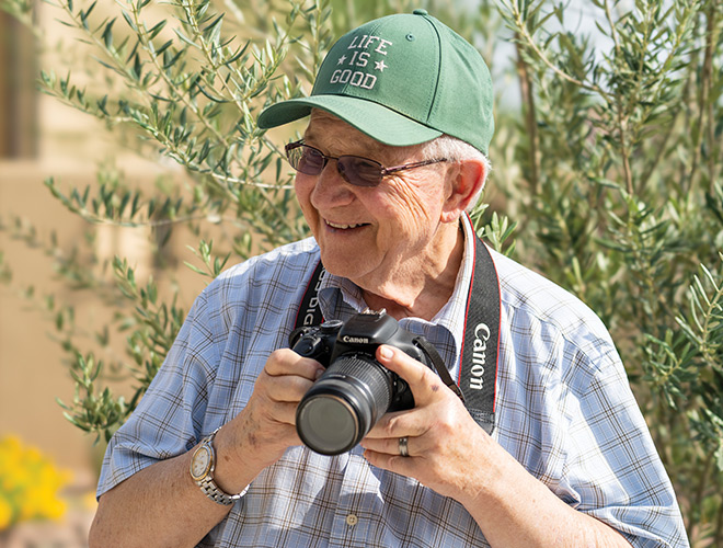 A resident surrounded by trees wearing a green baseball cap and holding a camera  