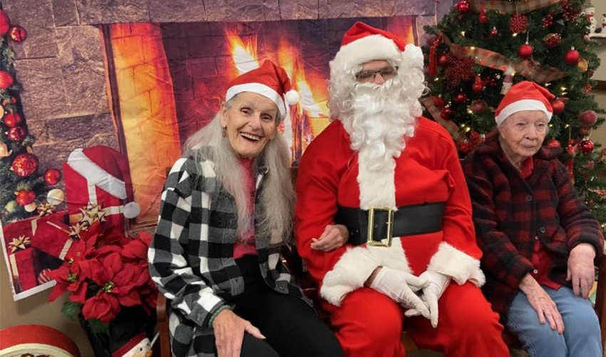 Two people sitting with Santa in front of a fireplace.