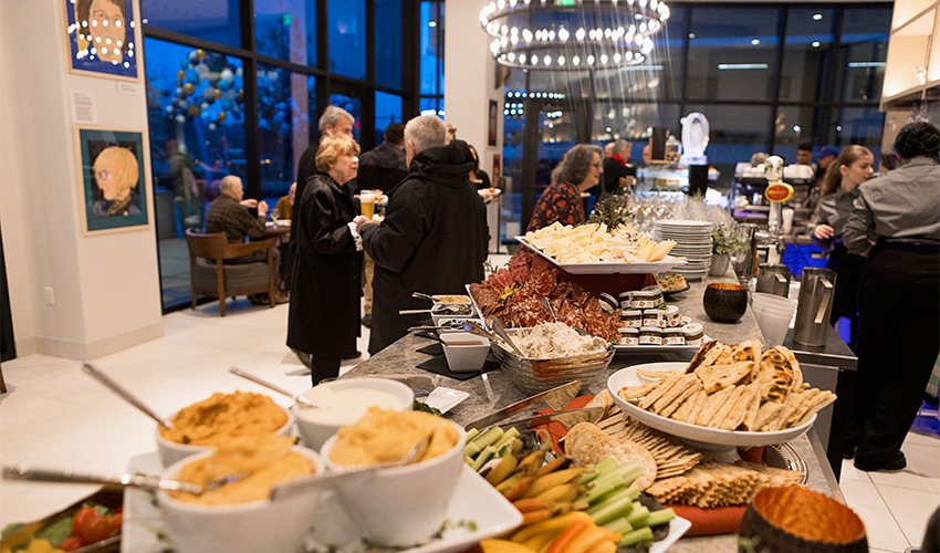 A table full of food at an event with people.